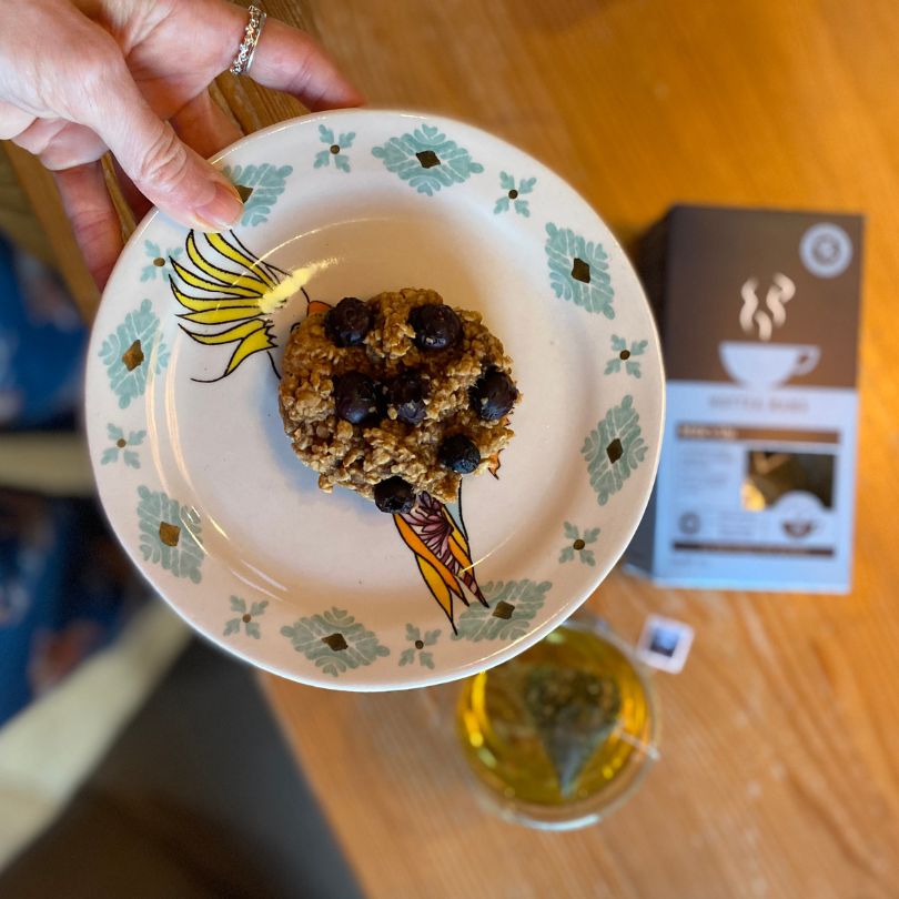 Blueberry lactation cookie on plate held above a table with HotTea Mama Milk's Up breastfeeding tea on the table below