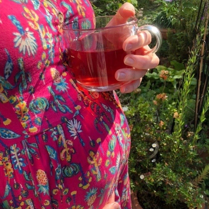 Pregnant lady wearing pink floral dress, holding a cup of get up and glow fruit tea