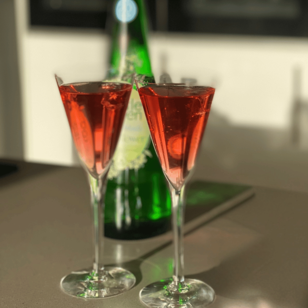 IMage of two cocktail glasses containing a Get Up & Glow Reviver in front of a bottle of elderflower fizz