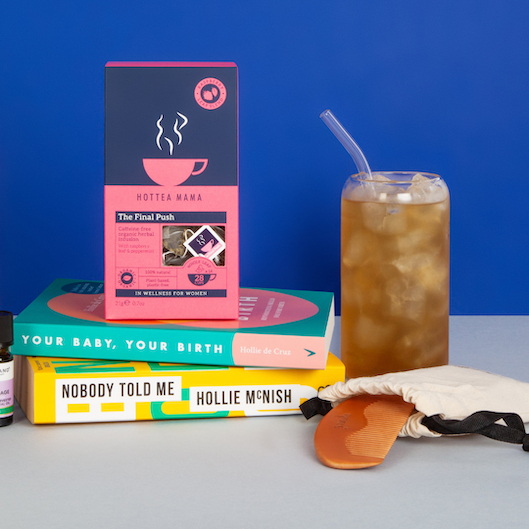 A blue background with birth preparation books and a birth comb on the side, next to a pack of HotTea Mama's The Final Push raspberry leaf tea and a glass of iced raspberry leaf tea with a straw