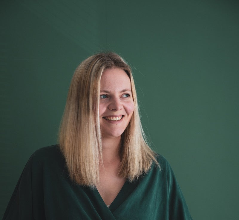 Blonde woman in green shirt, standing against a green wall