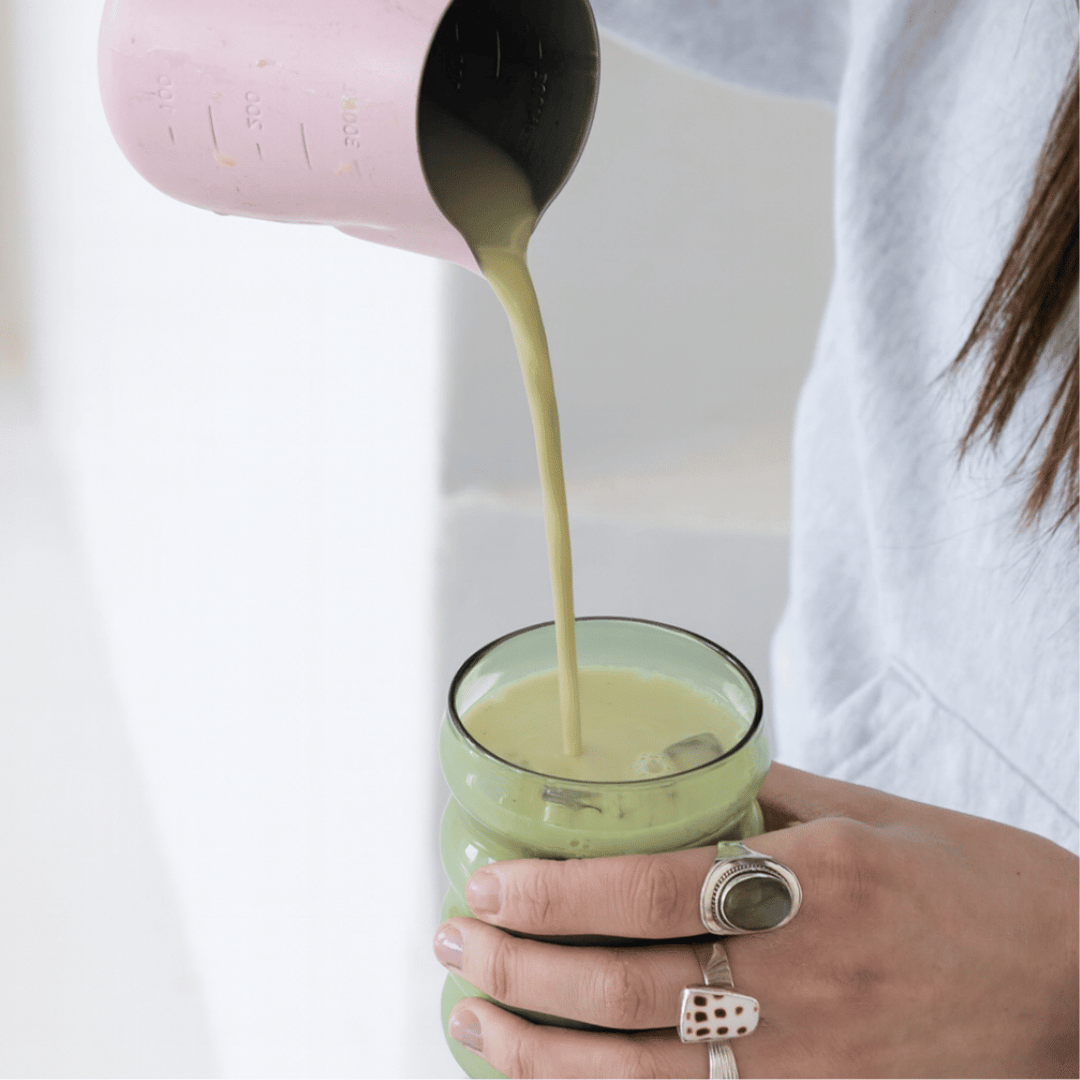 Matcha pouring from a pink jug into a glass, held by a woman wearing rings