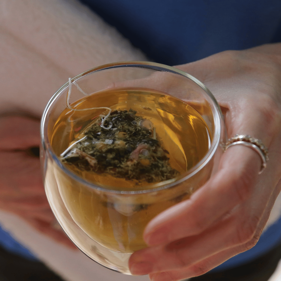 Image of a cup of tea being held in one hand and a hot water bottle in the other hand