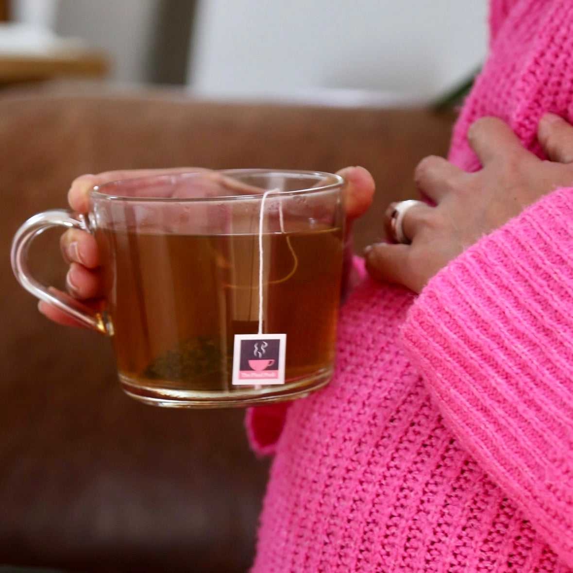 Pregnant woman wearing pink jumper holding a cup of raspberry leaf tea with a tea tag with HotTeea Mama logo and name of tea - The Final Push, on it