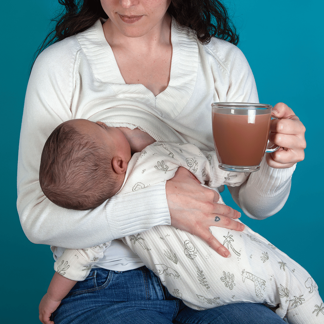 Image of a breastfeeding mother and her baby, holding a cup of Go With The Flow Lactation Support hot chocolate