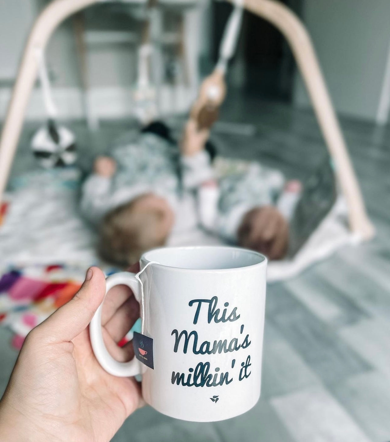 Babies on a play mat with mum watching while holding a cup of tea saying 'this mum's milkin' it'