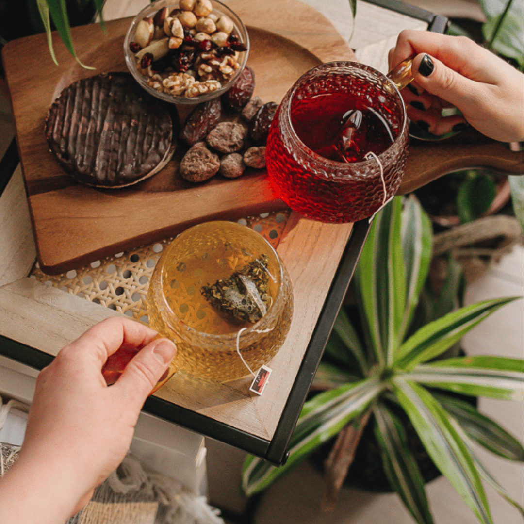 Image of two cups of brewed HotTea Mama herbal infusions being shared next to some healthy snacks