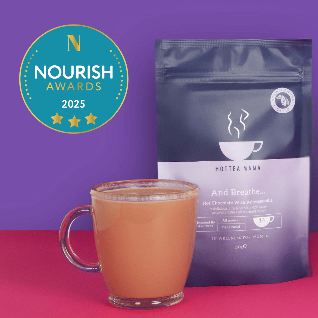 Hot tea in a glass mug with a pack of Hot Tea Mama And Breathe Ashwagandha hot chocolate on a purple background, featuring the Nourish Awards logo.