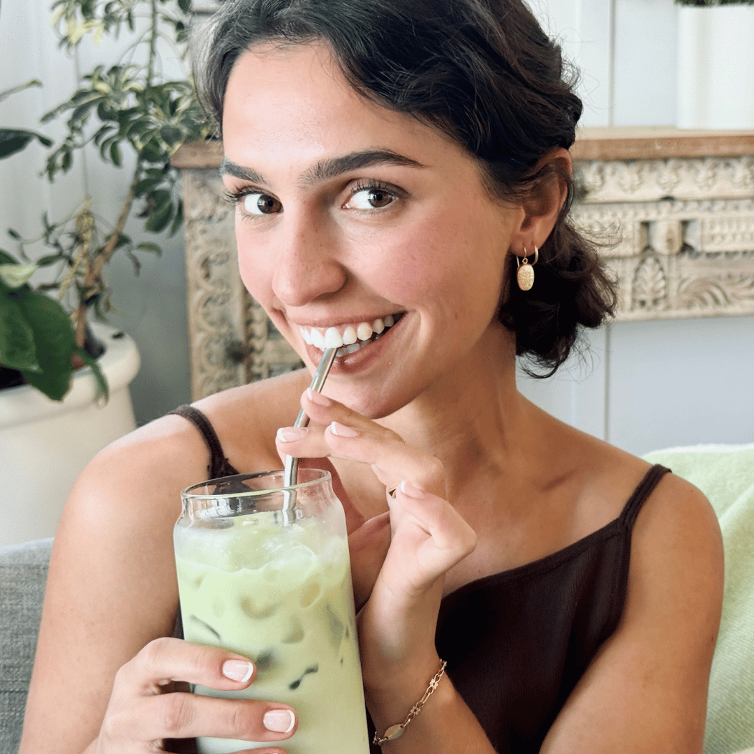 Woman enjoying an iced Mind Over Matcha with a straw in a cozy indoor setting.