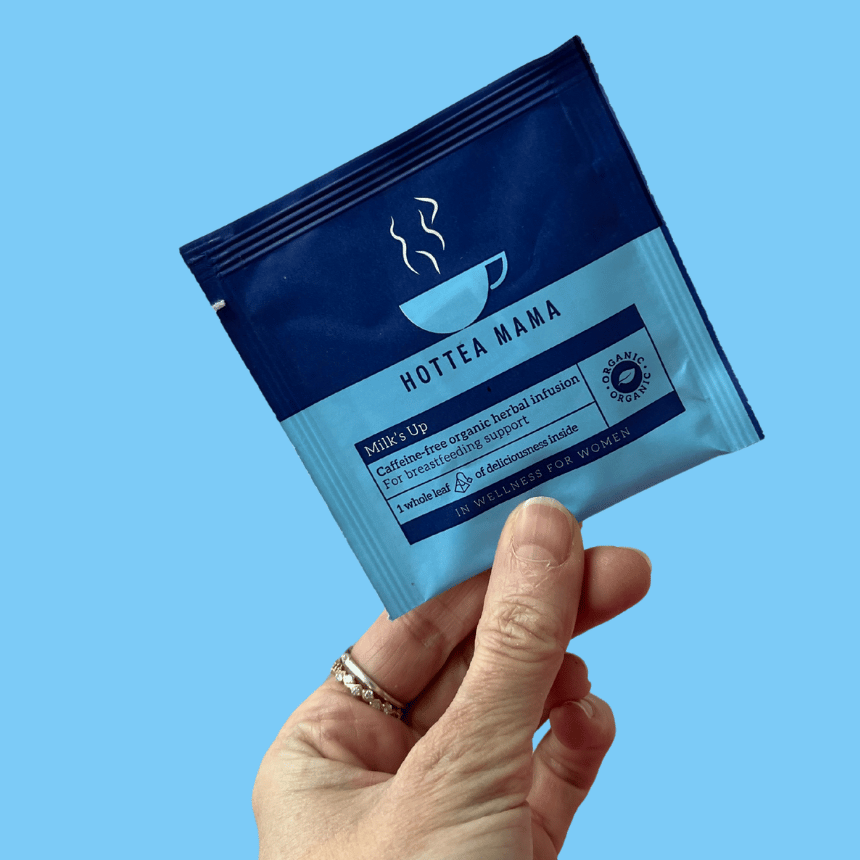 HotTea Mama Organic Milk's Up sample held by a hand on a blue background, showing it is the perfect way to try this mutli award winning caffeine free herbal tea blend for breastfeeding support