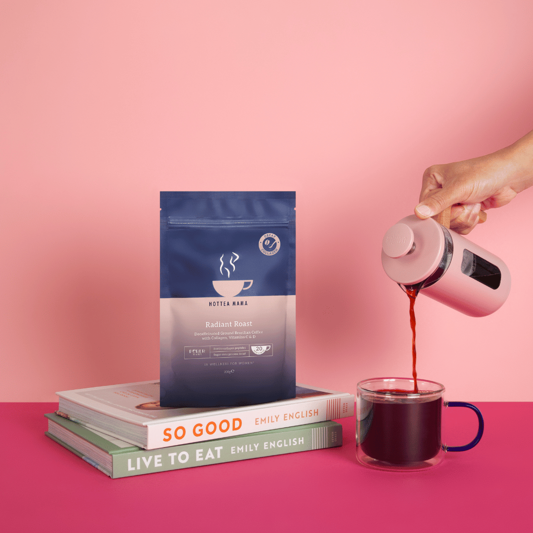 Hand pouring coffee into a mug with a coffee bag and books on a pink background