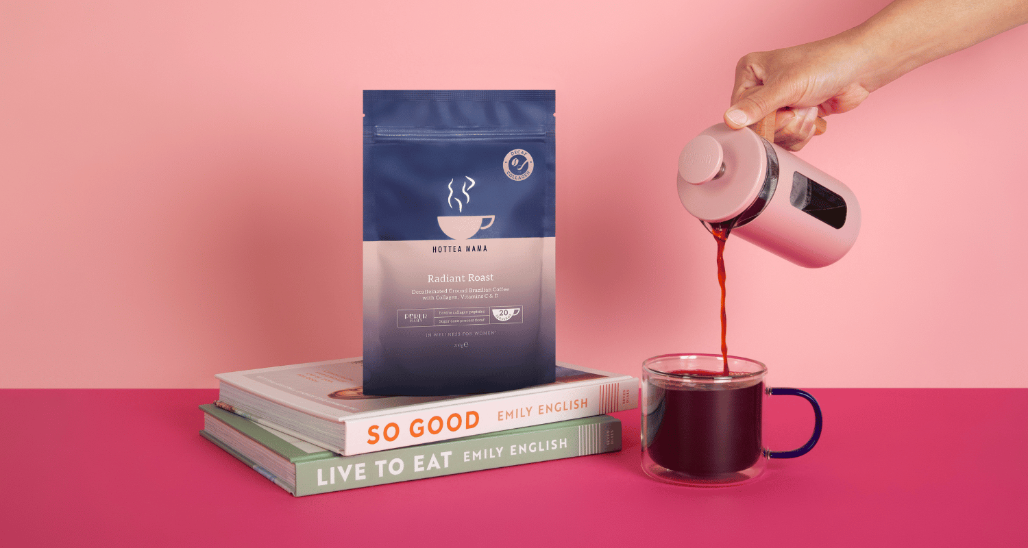 Person pouring HotTea Mama decaf collagen coffee into a mug with a package of coffee and books on a pink background