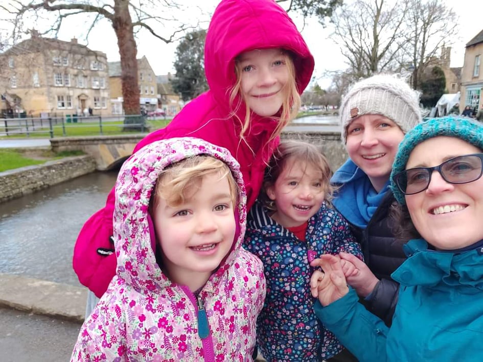 3 little girls and their 2 mums, hugging outside in rain jackets