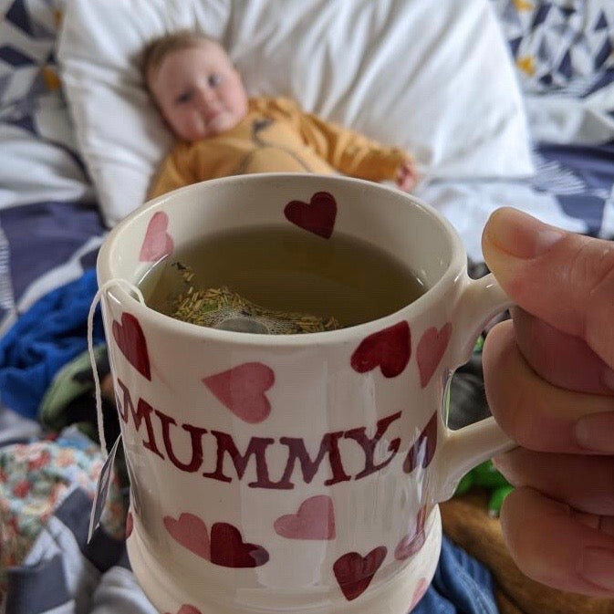 Mug with raspberry leaf tea in, close to the camera and baby in background