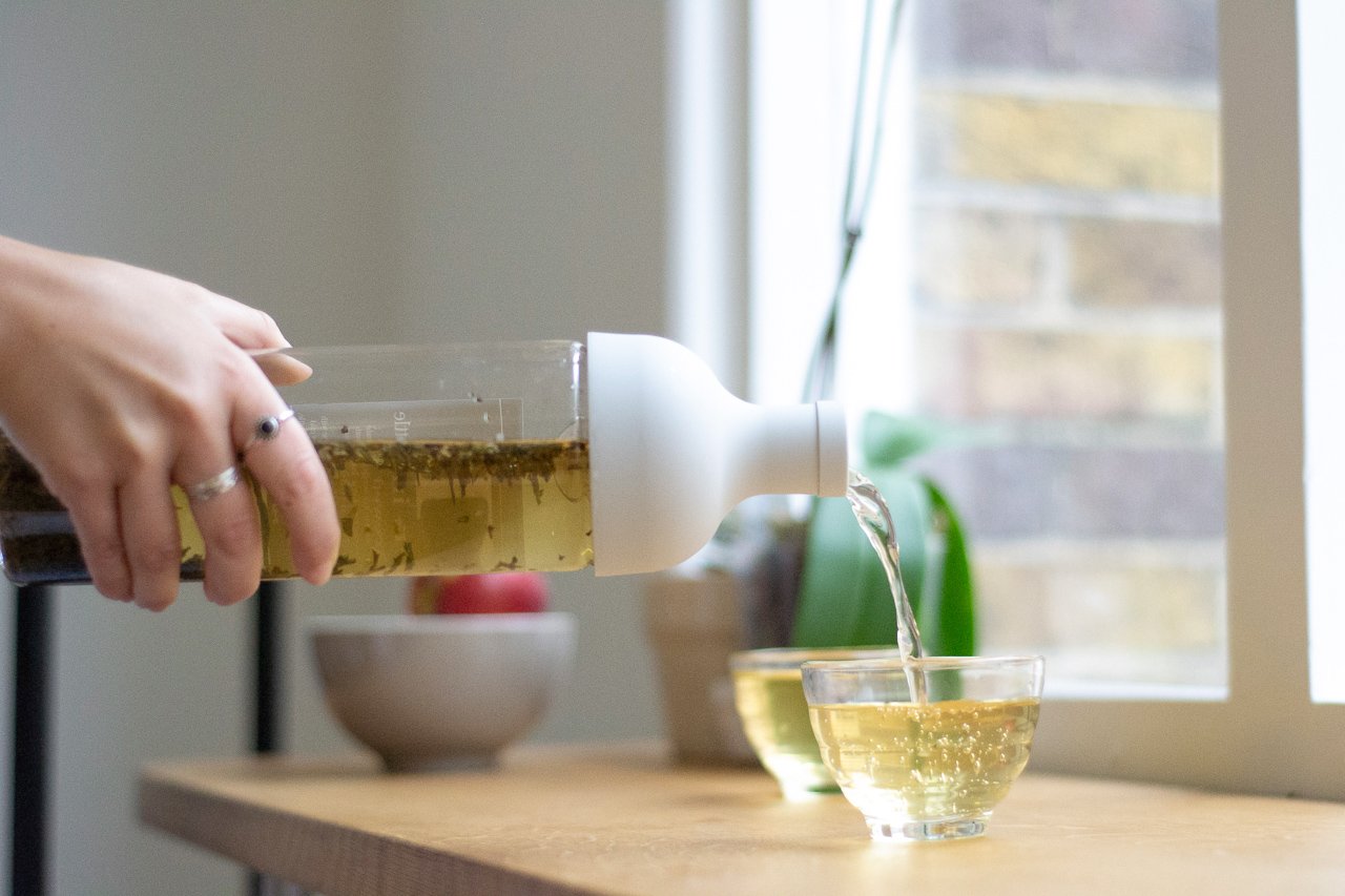 Bottle of iced tea being poured into a glass cup on a table by the window