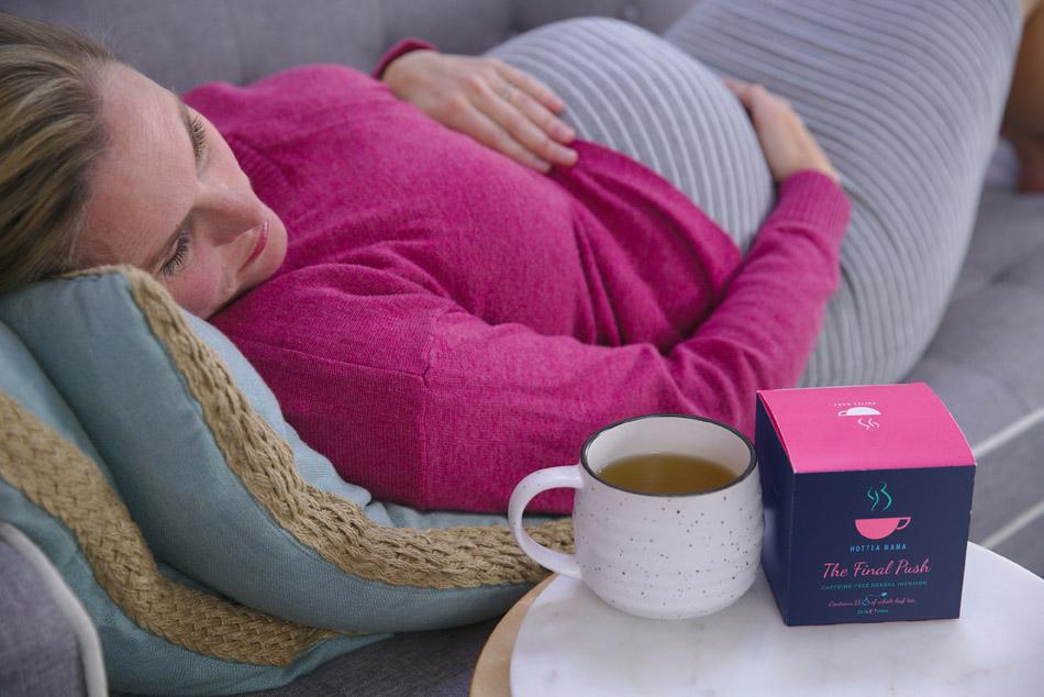 Pregnant woman lying down on sofa with a cup of The Final Push raspberry leaf tea