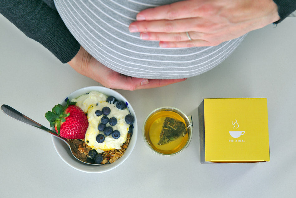 Downward facing shot over pregnant ladies belly showing muesli, brewed tea and tea box