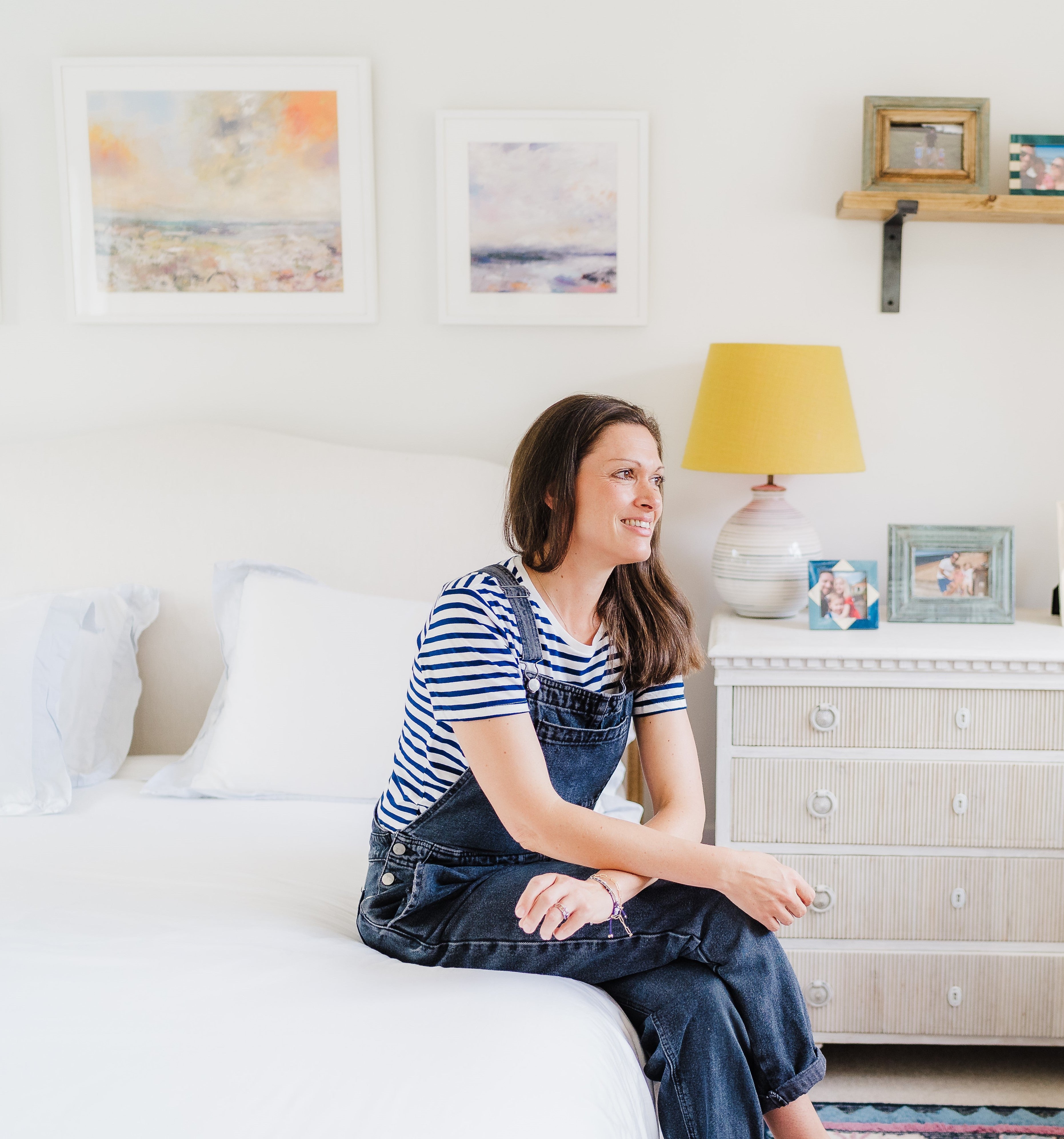 Woman in dungarees, sat on side of bed