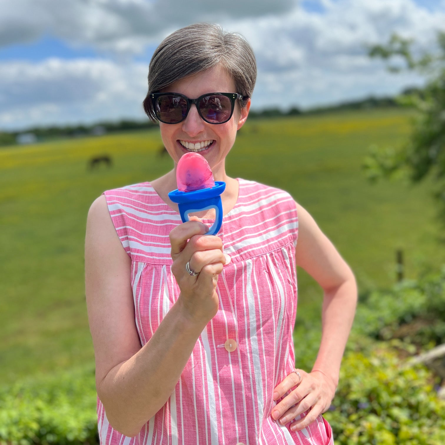 Woman stood in sunny garden, holding a Get Up And Glow iced lolly and smiling