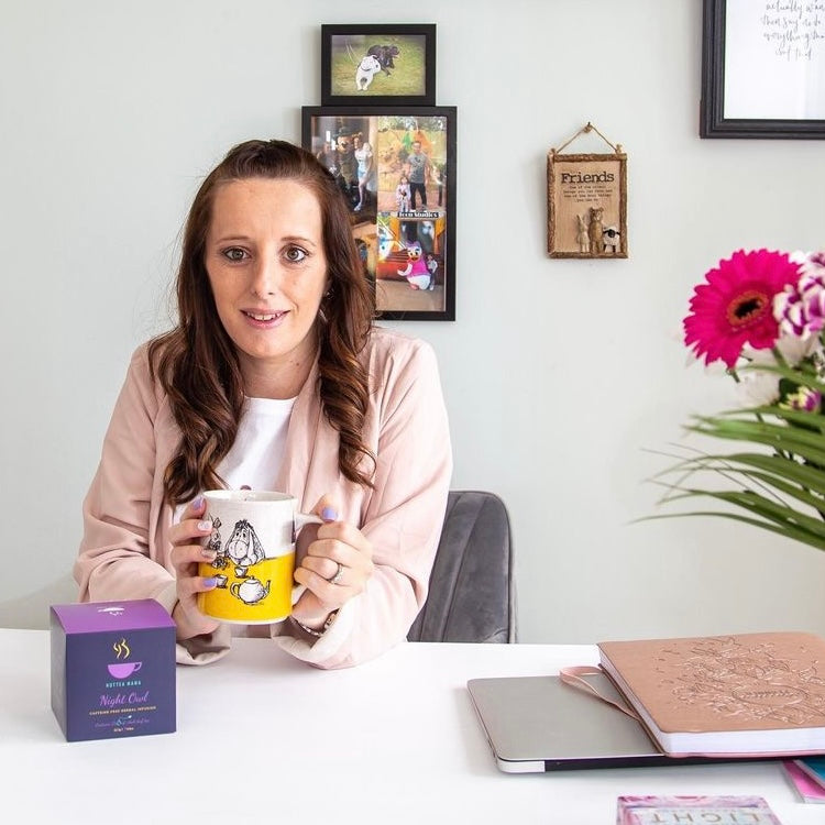 Woman sat at desk with laptop, books and a cup of tea