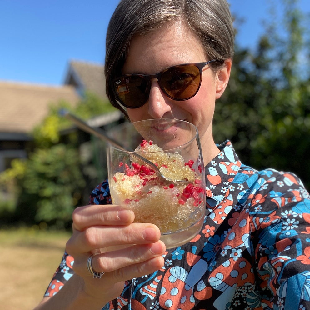 Woman wearing sunglasses, holding glass of iced tea granita with raspberries in it.