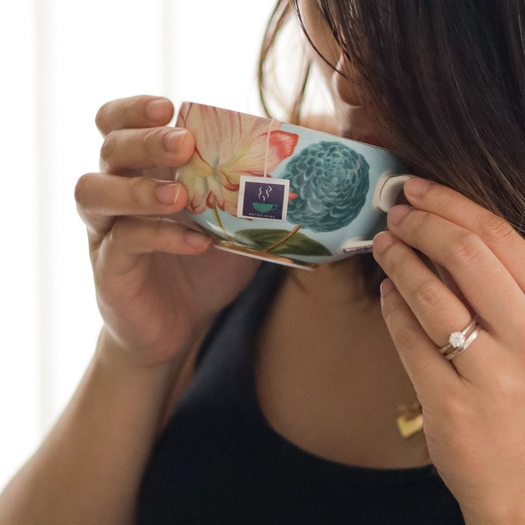 Lady holding cup of tea with HotTea Mama tea tag for raspberry leaf tea showing