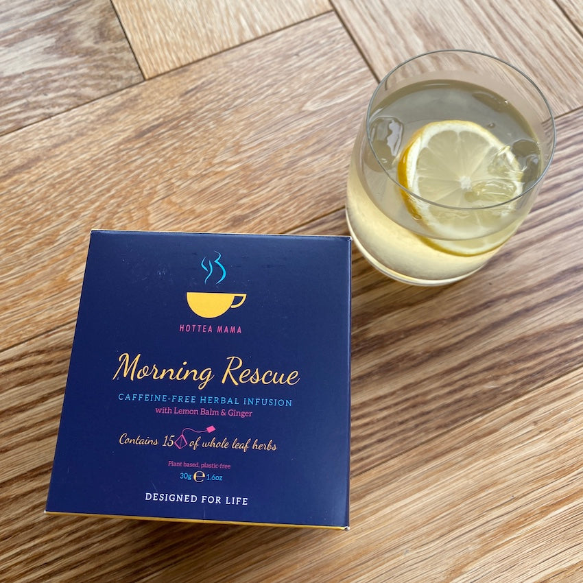 Morning Rescue tea box on wooden surface, next to glass of iced tea with lemon and ice in it