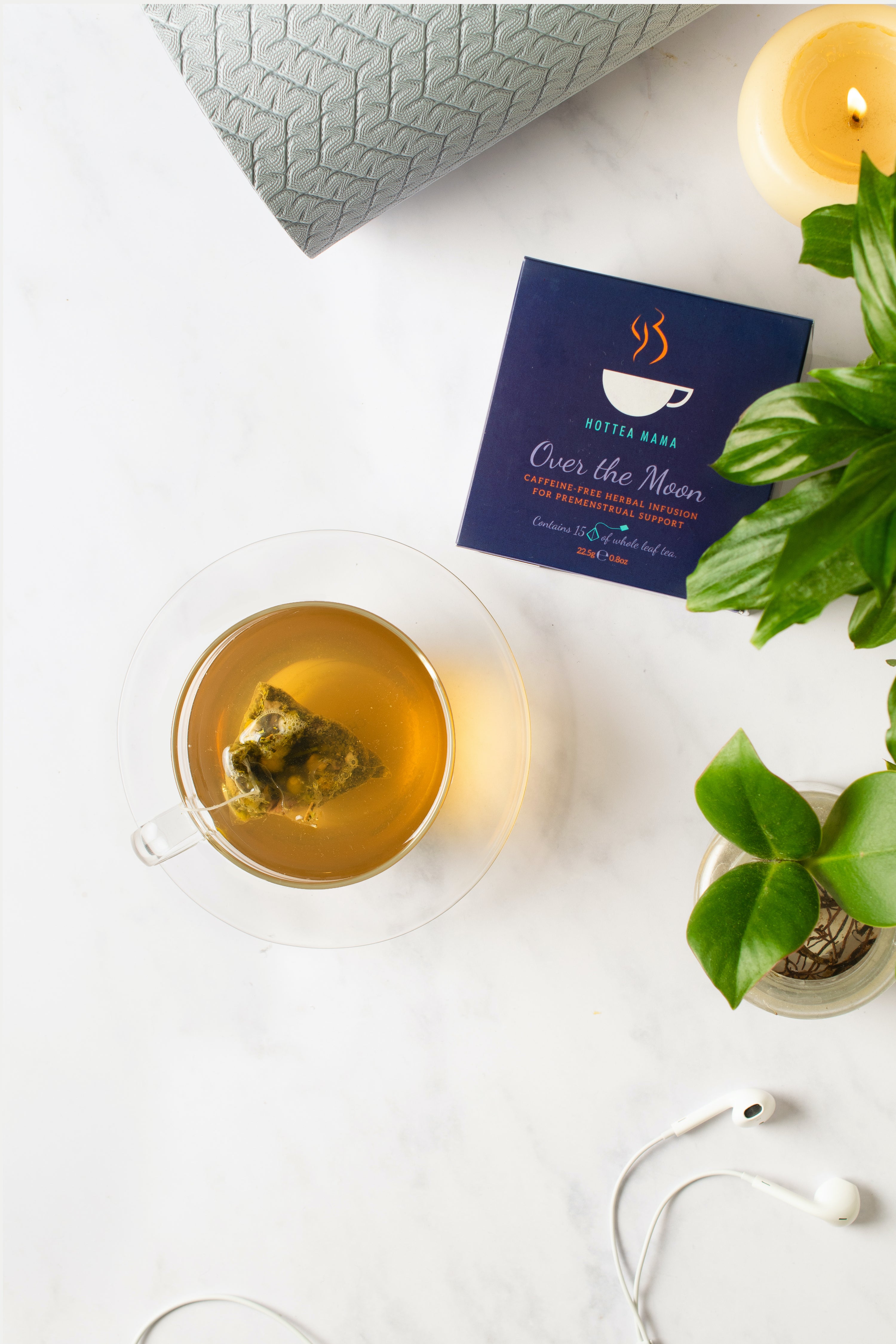 Brewed cup of over the moon tea in a glass cup, photographed from above with plant, yoga mat and headphones.