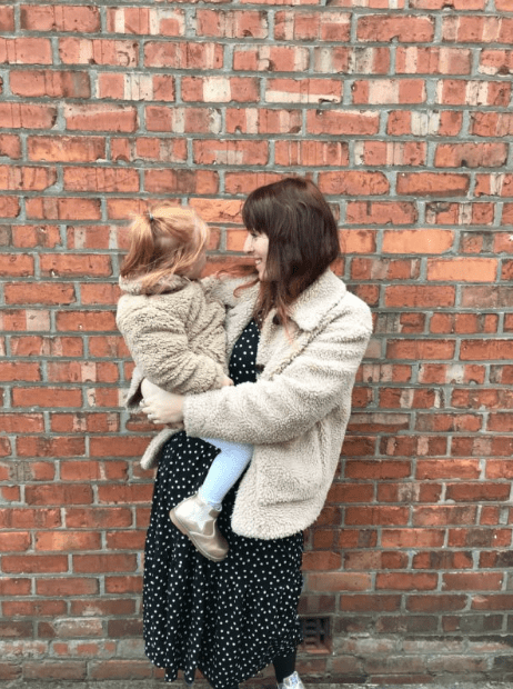 Emma, holding her daughter, stood in front of a brick wall