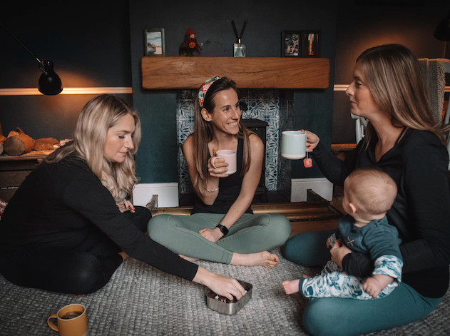 Group of mums with baby sat on rug, drinking tea