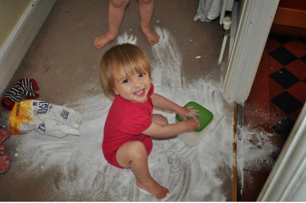Toddler rubbing icing sugar into a carpet while smiling