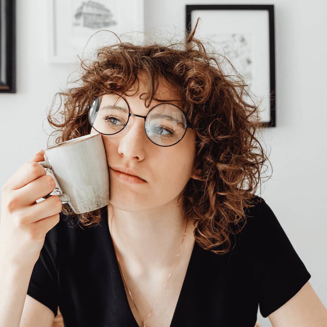 Image of a woman looking tired with a coffee cup pushed against her face