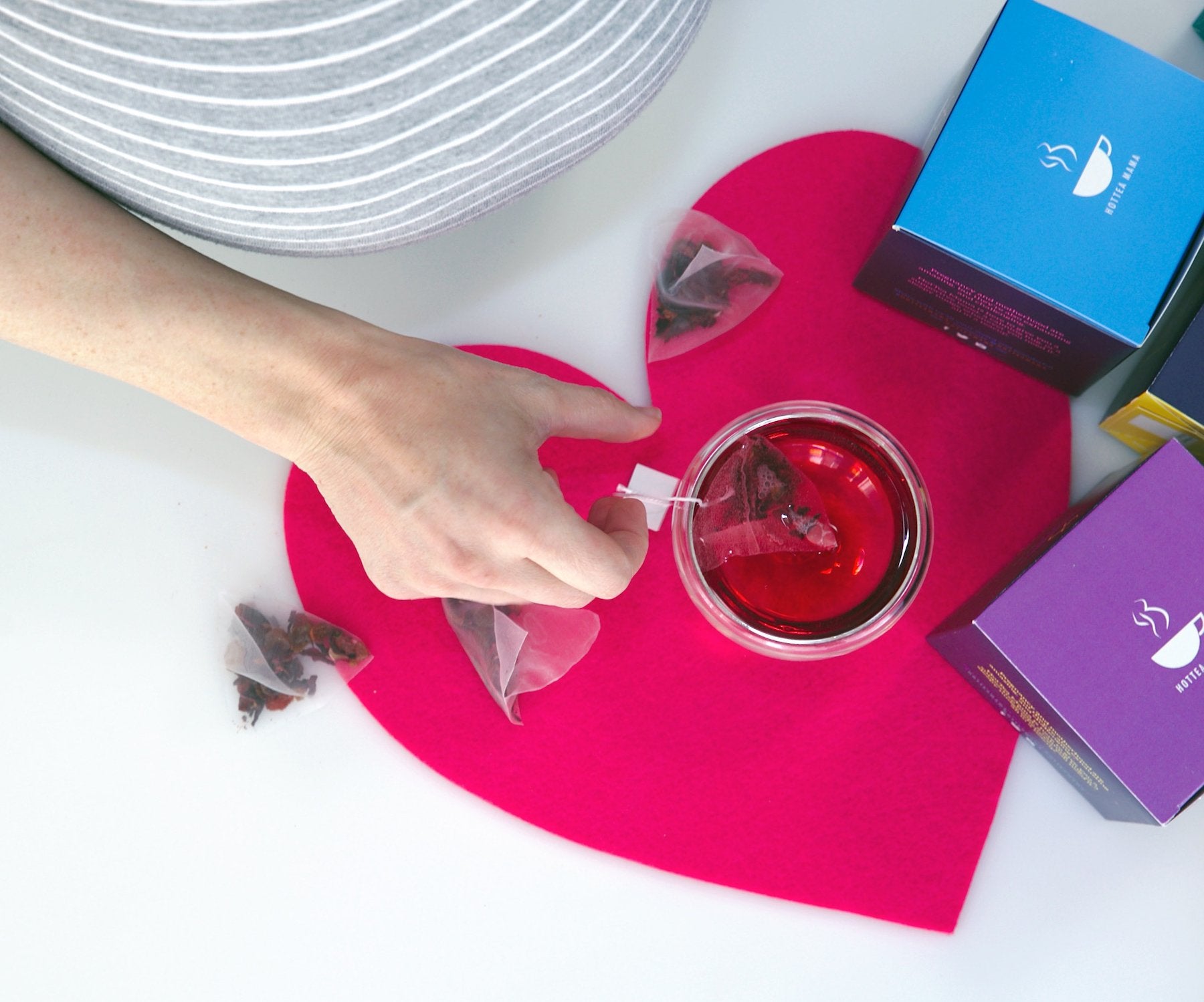 Cup of brewed tea on top of a love heart mat with pregnant lady holding cup