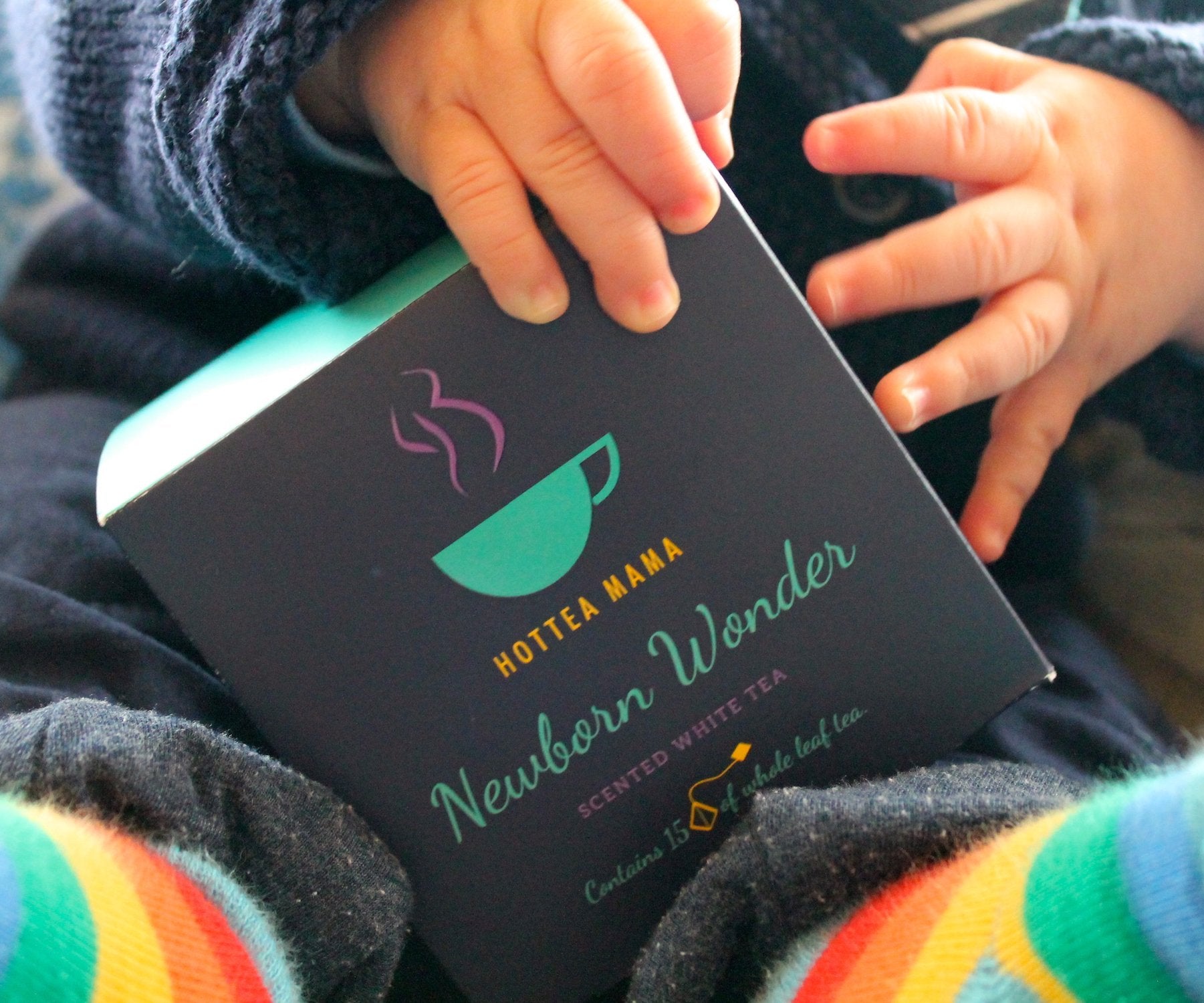 Close up shot of baby's hand and feet, holding onto a box of Newborn Wonder tea