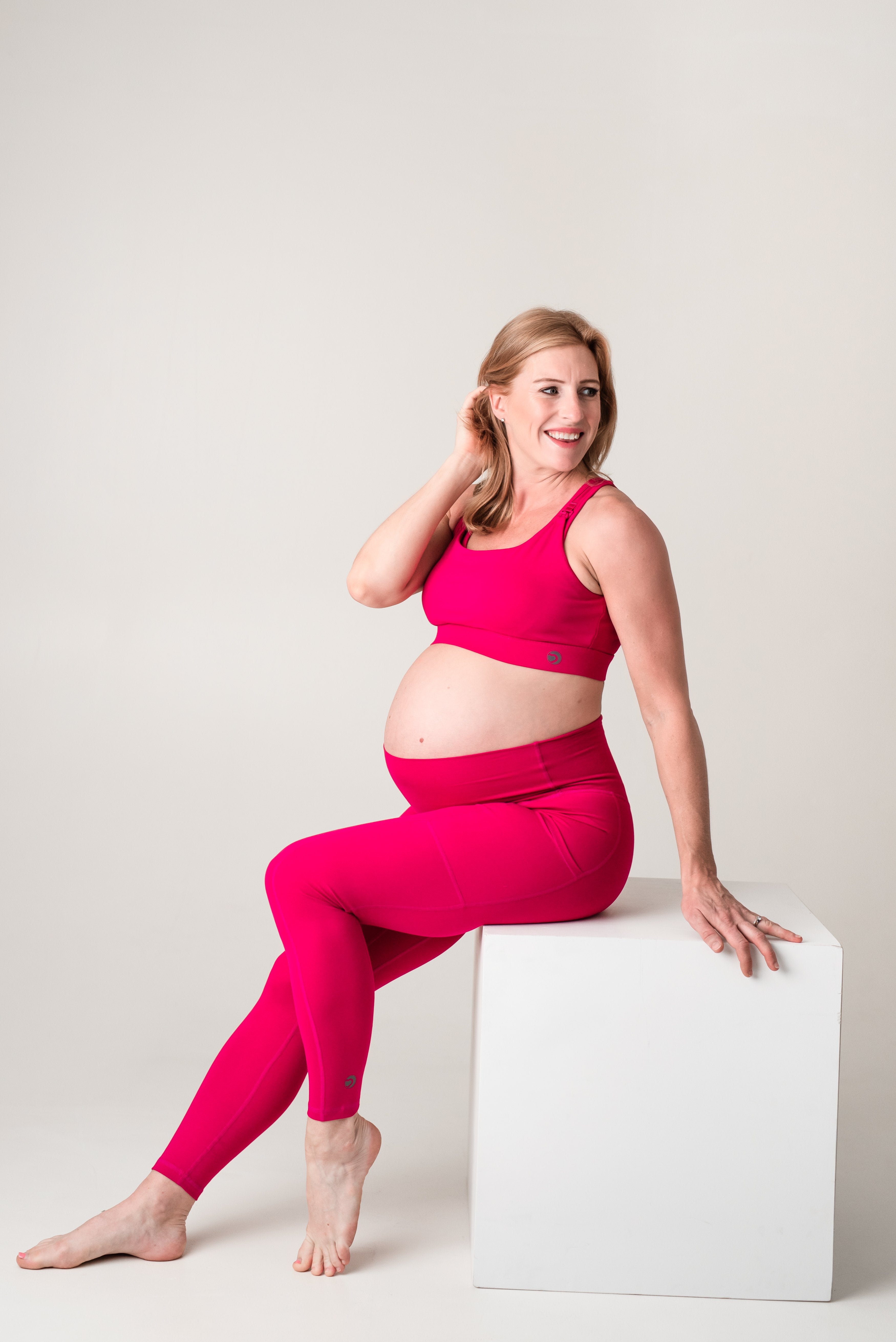 Pregnant Lady in pink sports wear leaning against a white block