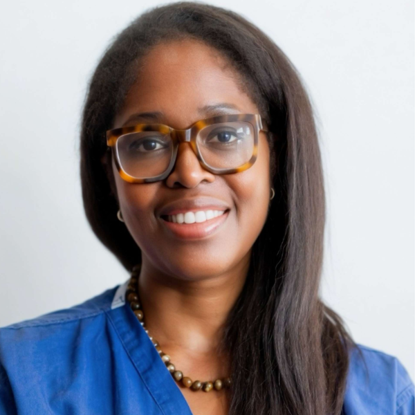 Woman wearing glasses and blue scrubs with a plain background