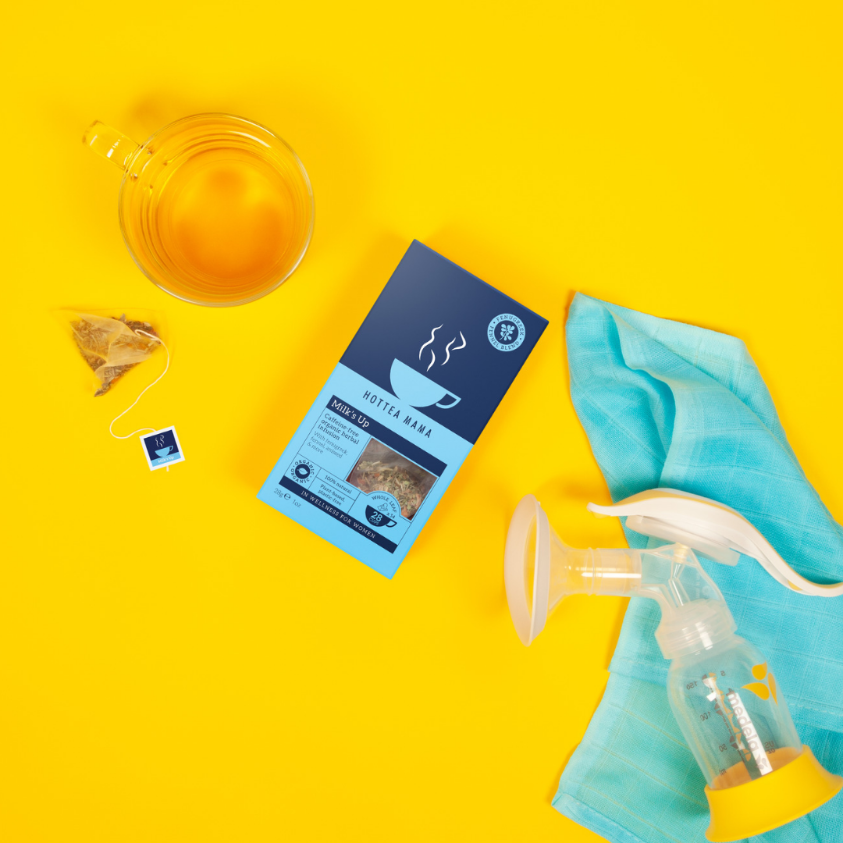 Flat lay image of HotTea Mama's Milk's Up breastfeeding tea on yellow background with a blue muslin, breast pump and brewed cup of lactation tea for nursing mums